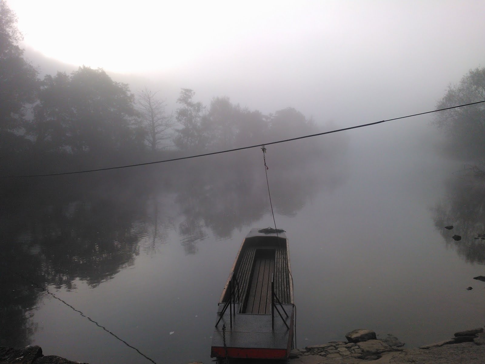 A ferry connected to a line crossing a river, foggy morning