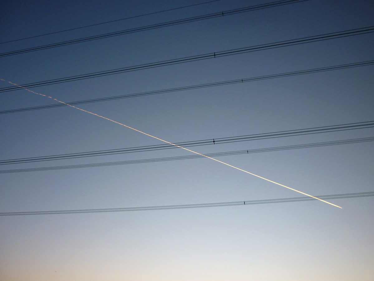 Power lines crossing a blue dusky sky, an aeroplane trail cuts across the lines